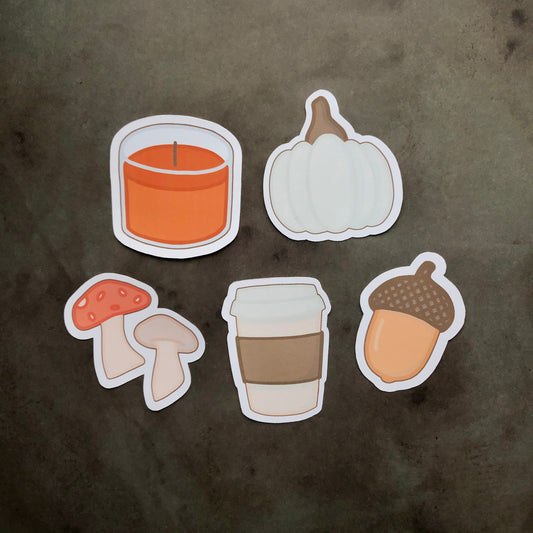 A set of five stickers featuring autumn-themed designs including a white pumpkin, two mushrooms, a coffee cup, and an orange candle.