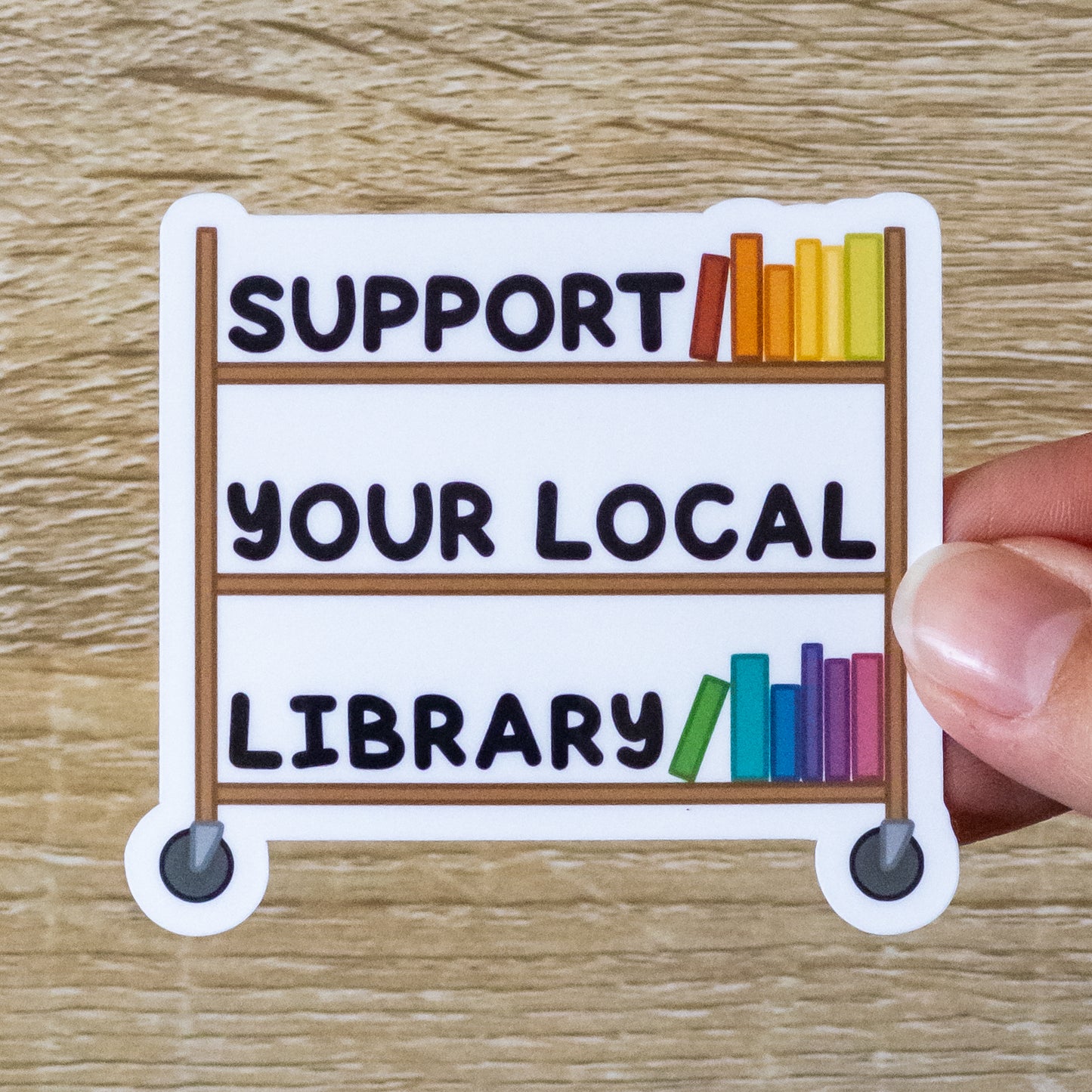 Glossy 2.8 inch wide sticker. Design is a wooden library book cart with several color books on it. Also sitting on the shelves is text that says, "Support Your Local Library"