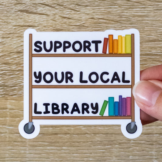 Glossy 2.8 inch wide sticker. Design is a wooden library book cart with several color books on it. Also sitting on the shelves is text that says, "Support Your Local Library"