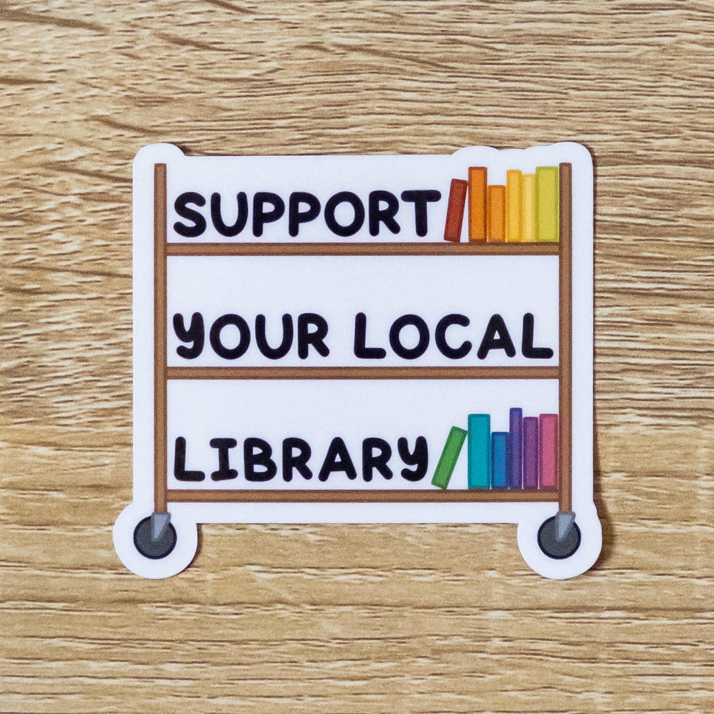 Glossy 2.8 inch wide sticker. Design is a wooden library book cart with several color books on it. Also sitting on the shelves is text that says, "Support Your Local Library"