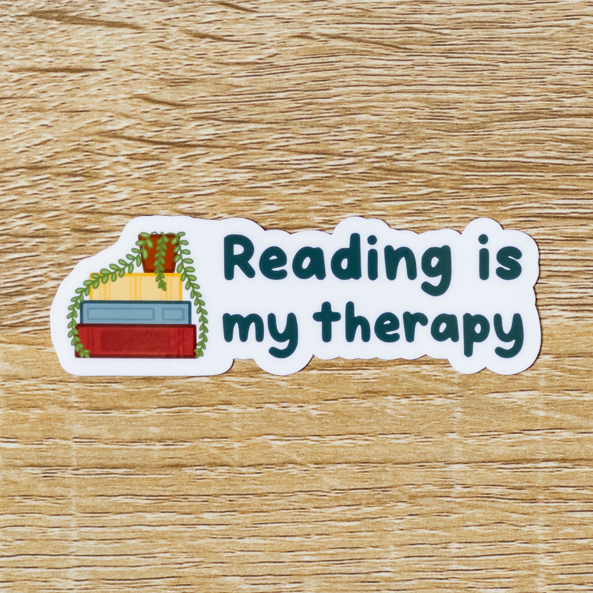 Glossy 3.6 inch wide sticker. Design is a stack of three books with a potted plant on top. The leaves drape over the red, yellow, and blue books. To the right, there is text that says, "Reading is My Therapy."