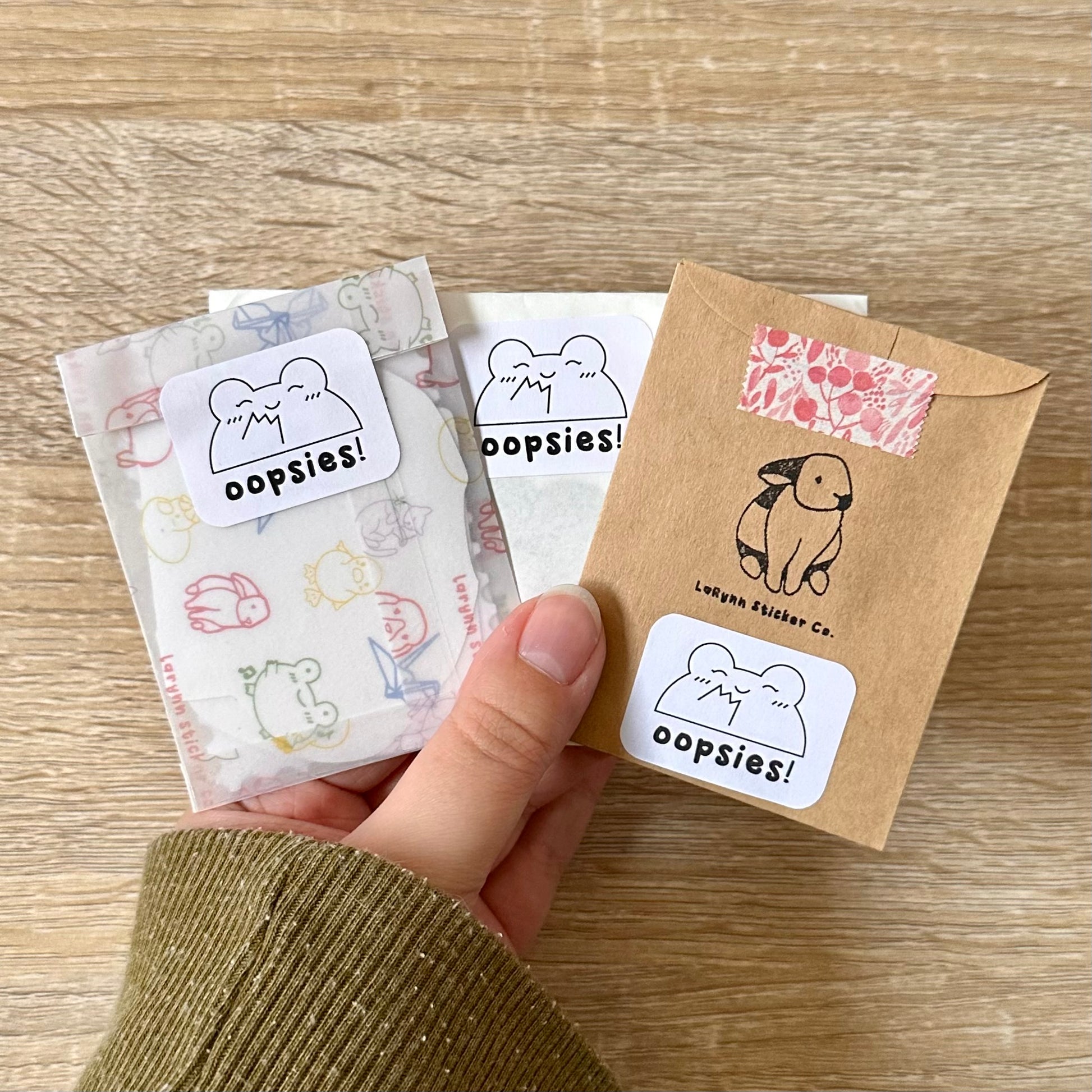 Holding three mystery packs of imperfect stickers. Each one is in different packaging. 