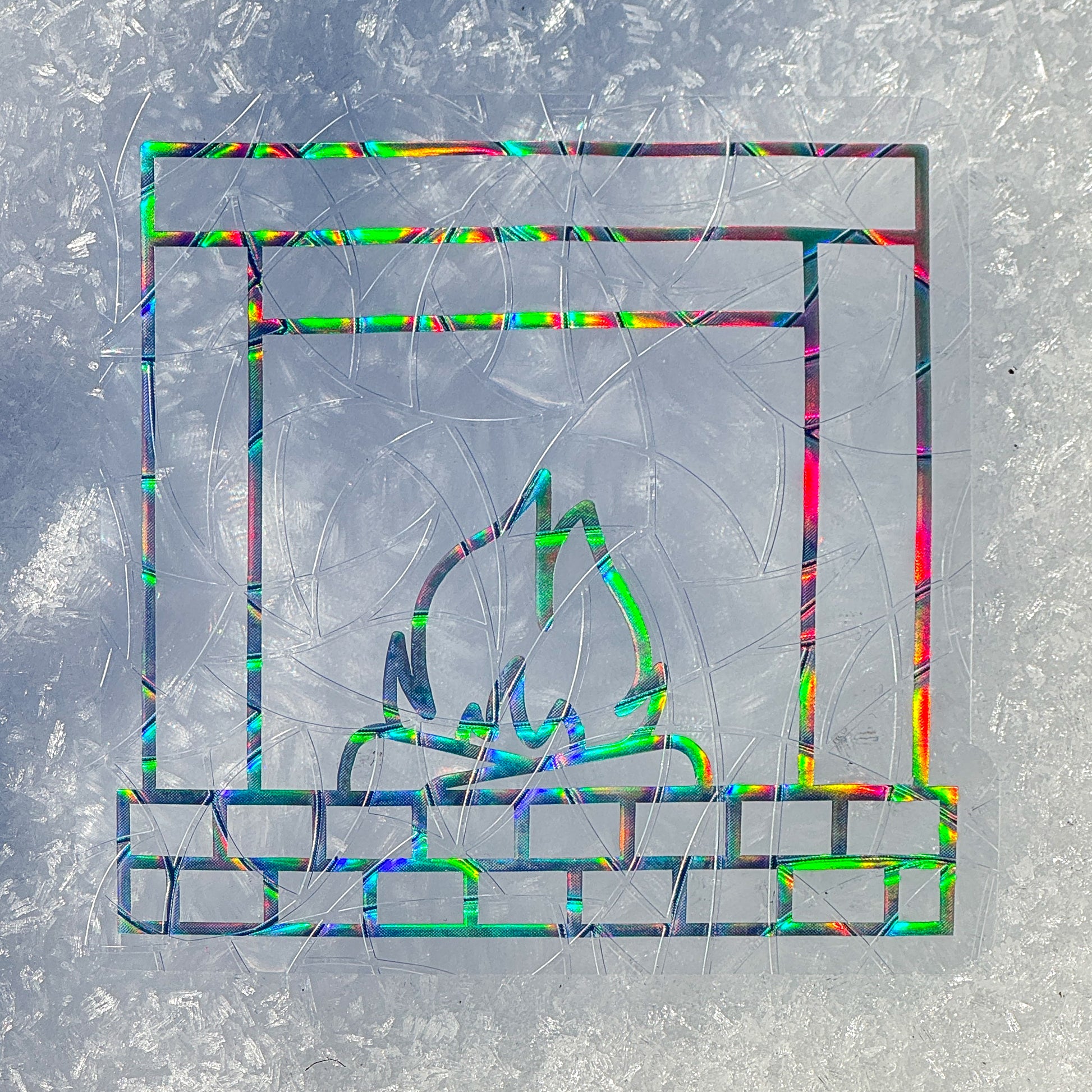 Holographic cozy winter fireplace suncatcher cling decal sticker. Holographic brick fireplace with two logs and a fire in the center. Laying against snow